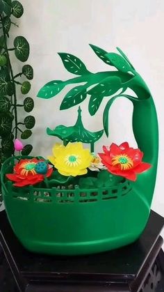 a green planter filled with flowers on top of a black table next to a potted plant