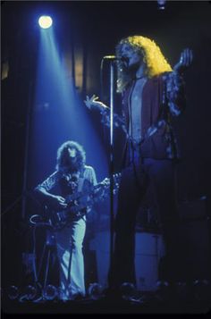 two people on stage with microphones in front of them and one person playing the guitar