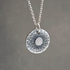 "Handmade sterling silver hammered disc necklace with a minimalist design. The pendant showcases a textured and oxidised surface, highlighting a small disc at its center. It gracefully hangs on a sterling silver trace chain. This symbolic handmade disc necklace serves as a reminder to find balance and stay centered. It makes the perfect gift for those seeking balance and harmony in their lives. With its meaningful design, it is especially cherished by yoga lovers and makes a thoughtful gift for friends, mothers, wives, girlfriends, or even as a special treat for oneself. Dimensions: Diameter of the disc approximately 1.5 cm (0.5\"). Metal: High quality 925 sterling silver The necklace will come in a beautiful branded gift box.  Each necklace is made by hand, ensuring that every piece posse Sterling Silver Coin Necklace With Oxidized Finish, Hammered Sterling Silver Coin Necklace, Hammered Round Sterling Silver Coin Necklace, Round Sterling Silver Hammered Coin Necklace, Hammered Silver Coin Necklace In Sterling Silver, Hammered Round Disc Minimalist Necklace, Minimalist Hammered Coin Necklace, Minimalist Hammered Round Disc Necklace, Minimalist Hammered Round Coin Necklace