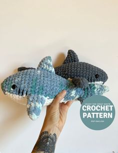 two crocheted stuffed sharks are being held in front of a white wall with the words crochet pattern below it