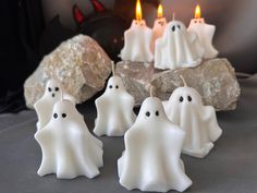 five white ghost candles sitting on top of a table next to some rocks and stones