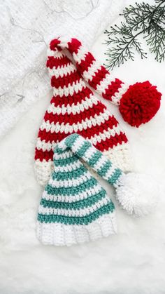 a crocheted hat and mitten laying on top of snow next to a fir tree