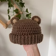 a hand holding up a brown crocheted bear hat