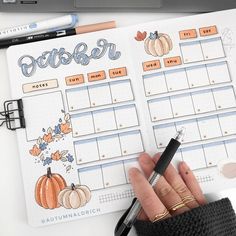 a person holding a pen in their hand next to a planner with pumpkins on it