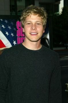 a young man standing in front of an american flag