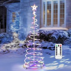 a lighted christmas tree in front of a house with a remote control on the ground