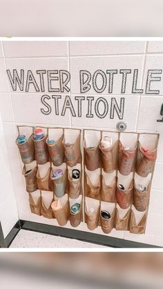 there is a sign that says water bottle station with many cups on the wall behind it