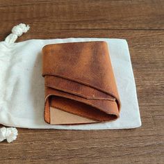 a brown leather wallet sitting on top of a wooden table next to a white cloth