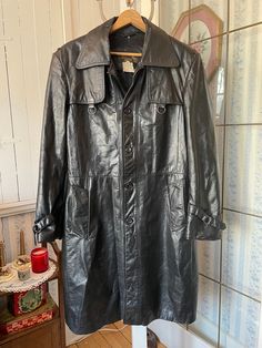 This classic black leather coat was made by the Hudson's Bay Ltd.'s Stores for Men. It fastens with buttons in the front and has two front pockets and tabs with buckles on the cuffs. The coat is lined with black quilted fabric lining. Marked size 42. The measurements, taken with the coat lying flat, are: shoulder to shoulder, 19 inches; armpit to armpit, 21 inches; sleeves, 26 inches; length, 45 inches; bottom edge, 40 inches. Please note that the coat has some marks and signs of wear; however, the coat overall is in fair vintage condition. Vintage Black Leather Jacket With Button Closure, Vintage Black Outerwear With Snap Buttons, Black Vintage Leather Jacket With Button Closure, Classic Vintage Black Winter Outerwear, Vintage Black Outerwear With Horn Royal Buttons, Black Vintage Outerwear With Double Button Closure, Vintage Black Leather Winter Outerwear, Vintage Black Leather Outerwear For Winter, Vintage Long Leather Jacket For Business