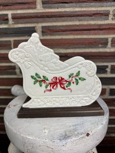 a white christmas sleigh with holly and red bow on it sitting on a pedestal