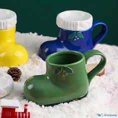 three plastic rain boots sitting on top of snow covered ground next to a toy house