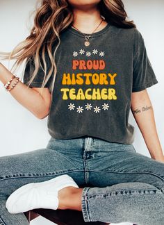 Celebrate a love of learning with our delightful Proud History Teacher Shirt! This adorable t-shirt is the perfect blend of cuteness and educational enthusiasm, making it an ideal gift for history teachers and a must-have for history teams gearing up for back-to-school season. Sure to be a favorite for teacher appreciation, gift giving, team t-shirts, and more! The breathable material ensures all-day comfort, while the durable construction ensures that this shirt will withstand the demands of an Retro Crew Neck T-shirt For Teacher Appreciation, Graphic Tee With Slogan For Teacher Appreciation, Graphic Tee Shirt With Slogan For Teacher Appreciation, Funny Cotton T-shirt For Teaching, Cotton T-shirt With Funny Print For Teacher Appreciation, Graphic Tee With Text Print For Teaching, Casual Tops With Funny Text For Teaching, School Spirit Letter Print Top, Graphic Print Short Sleeve T-shirt For Teacher Appreciation