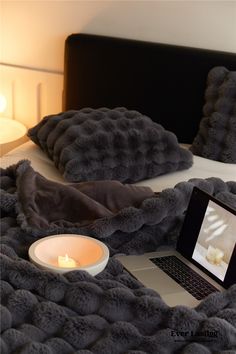 an open laptop computer sitting on top of a bed next to pillows and a candle