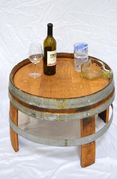 a wine bottle and two glasses sitting on top of a wooden barrel table with white background