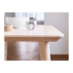 a wooden table with a white bowl on top of it and a glass in the background