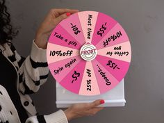 a woman holding a pink wheel of fortune with words written on the front and sides