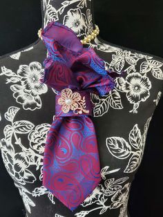 This  Blue and Red Paisley Necktie Necklace is made with a (Barry Wang) woven silk tie, and features a Rose Gold Pearl Flower Brooch strung on your choice of an adjustable Rosary Chain Ribbon Tie Pearl Necklace or an adjustable Elastic Band. The soft, comfortable fabric sits perfectly on any size chest, while the adjustable necklace feature allows you to customize the fit to your liking. Measuring at a versatile length, this necktie necklace is designed to be a one-size-fits-all. View all Women Neck Tie Necklace Diy, Elegant Multicolor Brooches For Formal Occasions, Elegant Multicolor Ties As A Gift, Elegant Multicolor Ties For Wedding, Elegant Multicolor Wedding Ties, Elegant Multicolor Suit And Tie Accessories For Wedding, Elegant Multicolor Wedding Suit And Tie Accessories, Elegant Purple Flower Brooch, Purple Flower Brooch For Formal Occasions