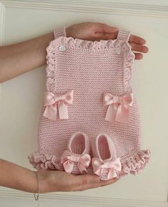 two hands holding a pink knitted baby outfit with bows on the front and bottom