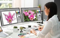 a woman sitting at a desk in front of two computer screens with flowers on them