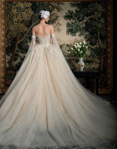 the back of a wedding dress with long sleeves and flowers on it, in front of a tapestry