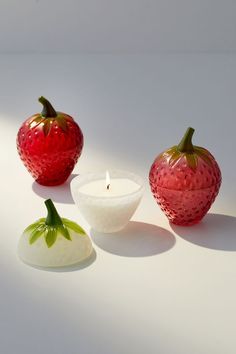 three strawberry shaped candles sitting next to each other on a white surface with one candle in the shape of an apple