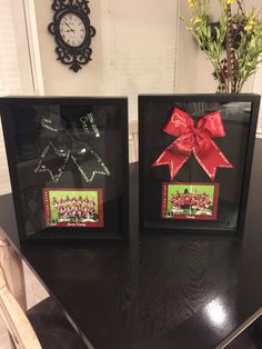 two black frames with red bows on them sitting on a table next to a clock