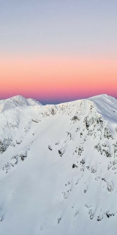 the mountains are covered in snow as the sun is setting over them and pink sky