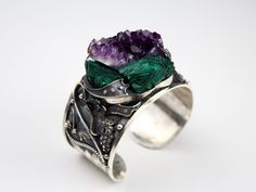 Introducing our exquisite Wide Cuff RAW Malachite Amethyst Sterling Silver Bracelet! This statement piece is a true fusion of natural beauty and contemporary style. Handcrafted with precision, the wide cuff design showcases the mesmerizing combination of raw Malachite and Amethyst gemstones set in gleaming sterling silver. Each stone is meticulously chosen for its unique markings, ensuring a one-of-a-kind piece that exudes luxurious elegance. With its adjustable fit, this bracelet effortlessly transitions from day to night, making it the perfect accessory to elevate any outfit. Embrace the healing properties and stunning allure of this extraordinary bracelet, a must-have for the modern woman with a taste for exceptional craftsmanship. Bracelet weight 89 gr. Wide Cuff Bracelet RAW Malachite Handmade Amethyst Cuff Bangle Bracelet, Natural Stones Bangle As A Gift, Unique Natural Stones Bangle As Gift, Unique Bangle With Natural Stones As Gift, Unique Bangle With Natural Stones For Gift, Unique Collectible Cuff Jewelry, Adjustable Gemstone Cuff Bracelet Collectible, Handmade Amethyst Bangle, Unique Amethyst Bracelet Jewelry