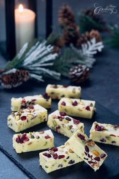 several pieces of white chocolate with nuts and dried cranberries on a table next to a lit candle