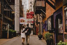 a man and woman are walking down an alley way in the middle of town together