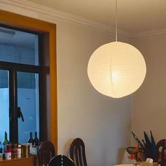 a dining room table with chairs and a lamp hanging from it's ceiling in front of a window