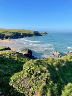 the beach is surrounded by green grass and rocks