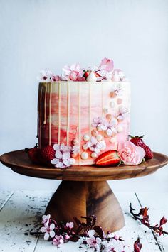 a pink cake with white icing and flowers on a wooden platter next to berries