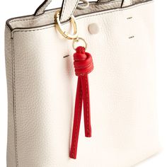 a white purse with a red ribbon on the handle and a key chain attached to it