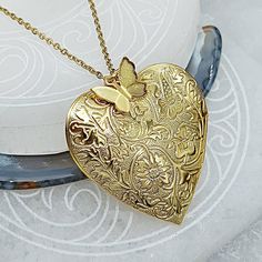 "Pretty gold tone embossed heart locket. A fillable glass vessel is tucked away inside to hold a special keepsake. Consider memorial ash, a lock of hair, small flower seeds, dried flowers, earth or sand or a clip of special cloth. This is a larger lightweight locket. The butterfly charm is included. There is room for a photo also. Measurements: *This is a larger style heart locket* It measures about 1 1/2\" tall x 1 1/2\" at widest part of heart *It is a lightweight locket* Includes: 1 locket Bu Gold Heart Necklace Nickel Free, Gold Etched Heart Jewelry, Gold Etched Locket Necklace, Gold Heart Necklace Nickel Free For Anniversary, Yellow Gold Etched Locket Necklace As Gift, Etched Heart Gold Jewelry, Gold Locket Necklace For Mother's Day, Antique Gold Necklace For Valentine's Day Gift, Gold Memorial Locket Necklace