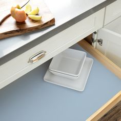 an open drawer in a kitchen with apples on the counter and cutting board next to it