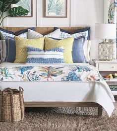 a bed with blue and yellow pillows on top of it next to a basket filled with fruit