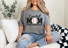 Elevate your casual style with this vintage baseball Mama t-shirt! Designed especially for Moms who are proud to cheer on their baseball stars! This soft and cozy tee features a unique black and white checkered design that perfectly frames the standout vintage style Mom baseball graphic. The blend of vintage vibes and modern flair makes this the ultimate shirt for game days, baseball tournaments, or simply showing off your baseball pride in everyday life.The Comfort Colors® 1717 ring spun cotton Varsity Cotton T-shirt For Baseball Season, College Sports Season T-shirt With Baseball Collar, College Baseball Collar T-shirt For Sports Season, Cotton Sports Fan Baseball Jersey, Cotton Baseball Jersey With Crew Neck For Sports, Cotton Crew Neck Baseball Jersey For Sports Events, Casual Cotton Baseball Jersey, Sports Season Graphic Print Top With Baseball Collar, Graphic Print Tops With Baseball Collar For Sports Season