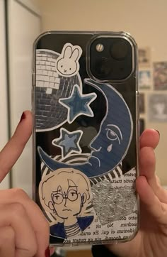 someone is holding up their phone case with stickers on it, and there are other things in the background