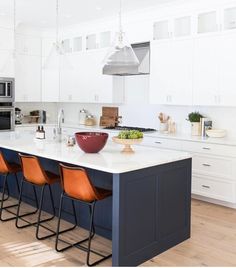 a kitchen with white cabinets and blue counter tops, orange chairs in front of the island