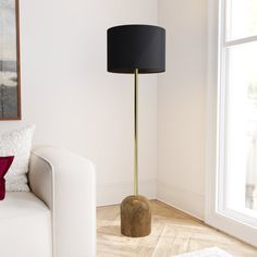 a living room with a white couch and a black lamp on the floor in front of a window