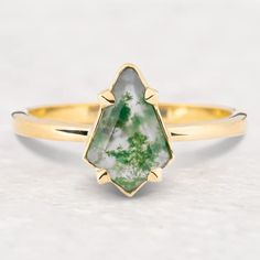 a gold ring with a green and white stone in the shape of a leaf on it