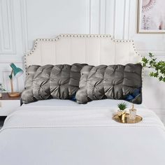 a white bed with three pillows on top of it and a plant in the corner