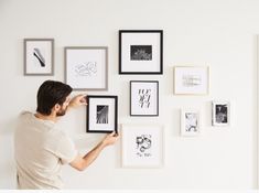 a man is hanging pictures on the wall with his hands and looking at them in black and white