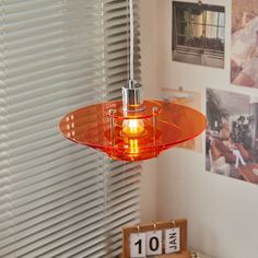 an orange glass light hanging from a ceiling in a room with pictures on the wall