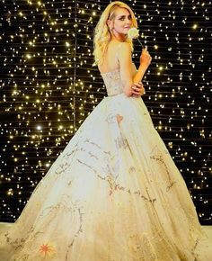 a woman in a white dress standing next to a wall covered with stars and lights