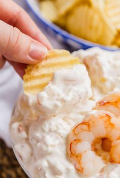 a person dipping shrimp into a bowl of cream cheese dip with crackers on the side