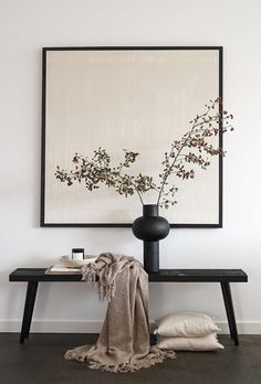 a black vase with flowers in it sitting on a table next to a white wall