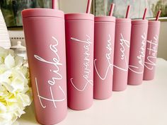 pink tumblers with white writing on them sitting on a table next to some flowers