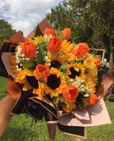 a bouquet of sunflowers and tulips is wrapped in brown paper on the grass